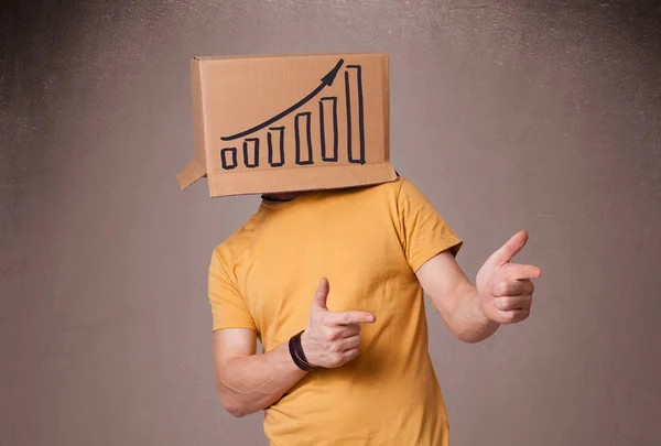 Young man gesturing with a cardboard box on his head with diagra — Stock Photo, Image