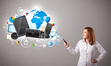 Genç bir kadın ayakta ve telefonunda geziniyor.