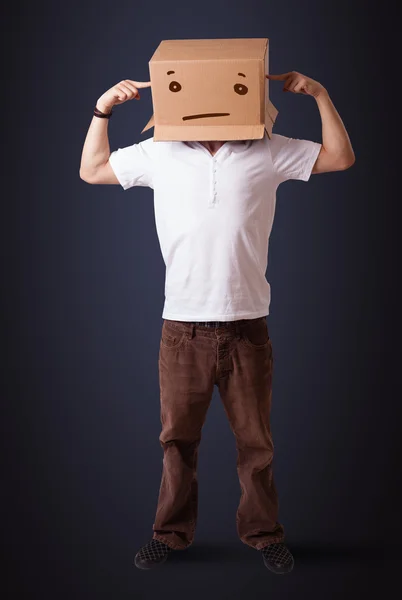 Joven haciendo gestos con una caja de cartón en la cabeza con straig —  Fotos de Stock