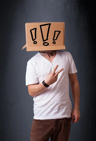 Young man gesturing with a cardboard box on his head with exclam — Stock Photo, Image