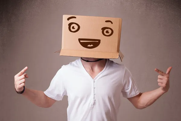 Giovane uomo che gesticola con una scatola di cartone in testa con un sorriso — Foto Stock