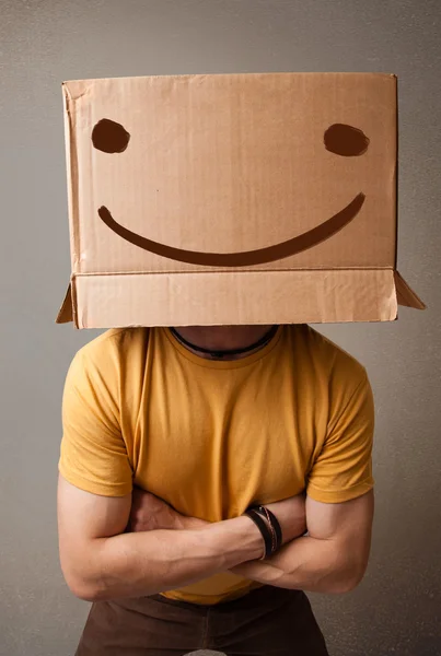 Young man gesturing with a cardboard box on his head with smiley — Stock Photo, Image