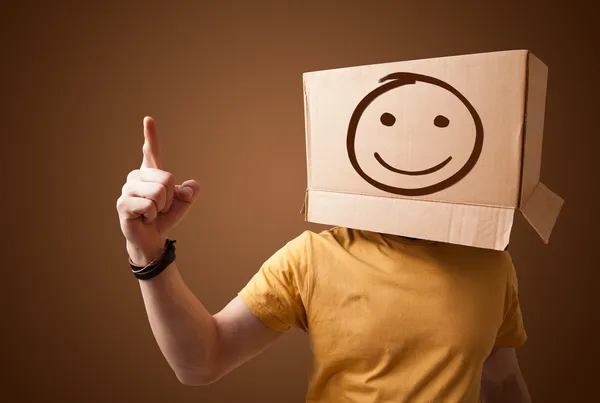Giovane uomo che gesticola con una scatola di cartone in testa con un sorriso — Foto Stock