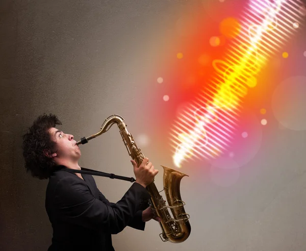 Молодой человек играет на саксофоне с красочными звуковыми волнами — стоковое фото