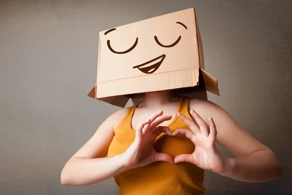Giovane donna gesticolare con una scatola di cartone in testa con smil — Foto Stock