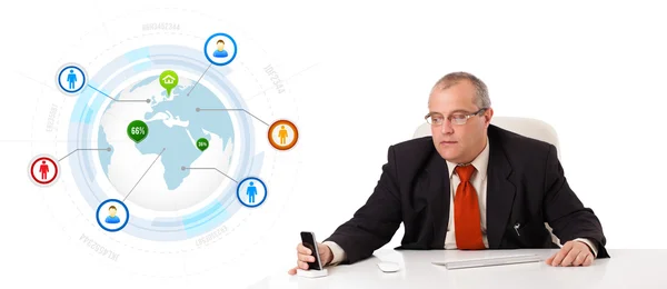 Businessman sitting at desk and holding a mobilephone with globe Stock Picture