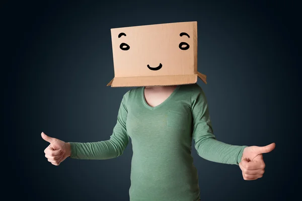 Mujer joven haciendo gestos con una caja de cartón en la cabeza con una sonrisa —  Fotos de Stock