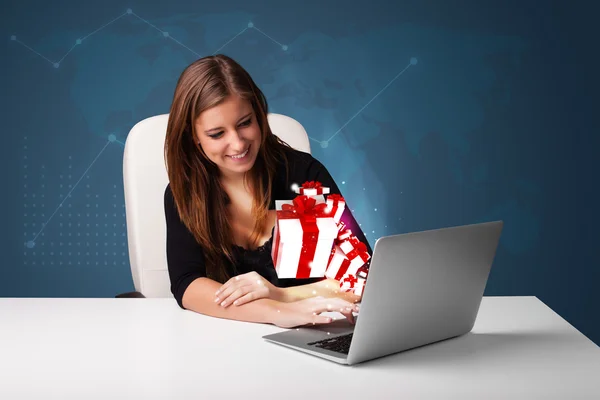 Pretty lady sitting at desk and typing on laptop with present bo — Stock Photo, Image