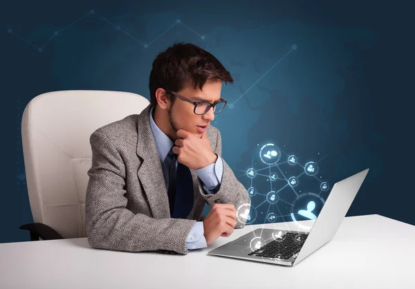 Jovem sentado na mesa e digitando no laptop com rede social — Fotografia de Stock