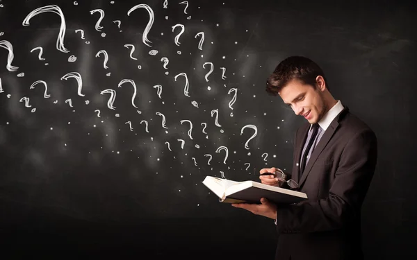 Young man reading a book with question marks coming out from it — Stock Photo, Image