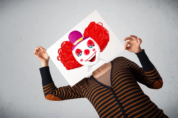 Woman holding a cardboard with a clown on it in front of her hea — Stock Photo, Image