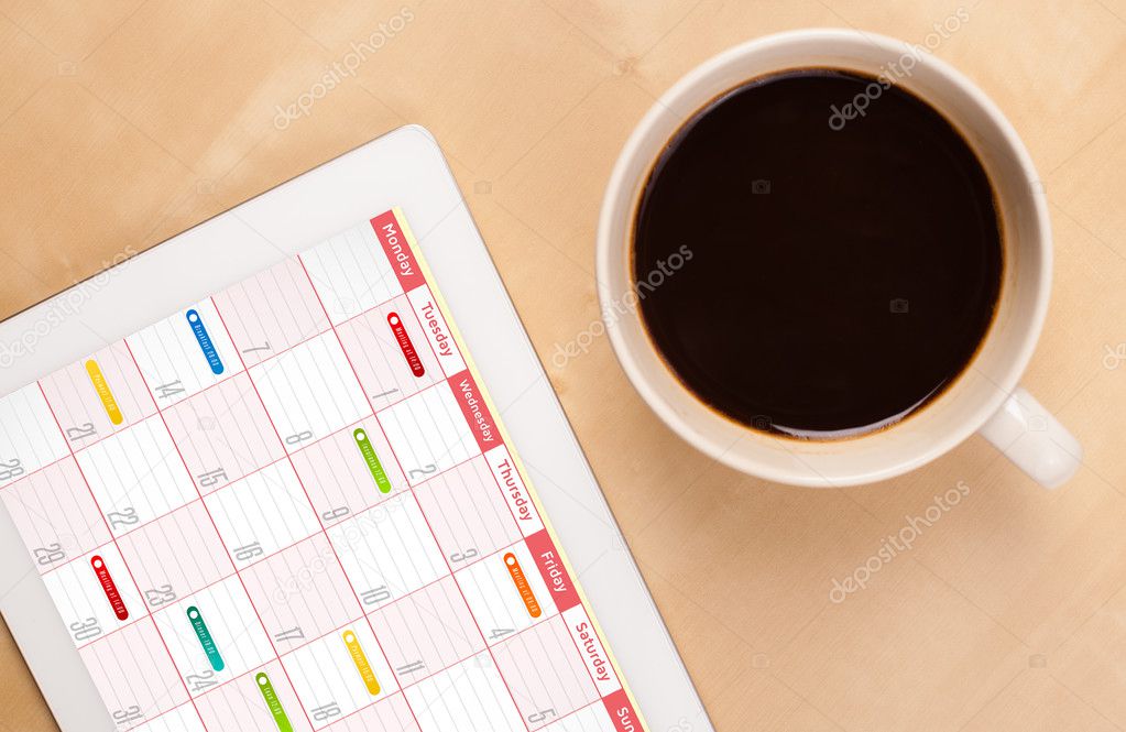 Tablet pc showing calendar on screen with a cup of coffee on a d