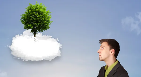 Молодой человек указывает на зеленое дерево на вершине белого облака — стоковое фото