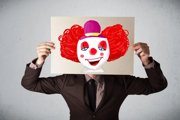 Biznesmen trzymając karton z clown na to przed h — Zdjęcie stockowe