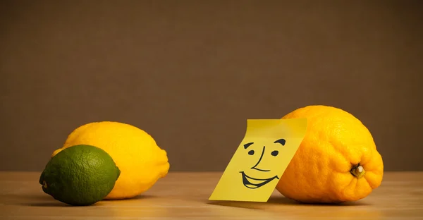 Lemon with post-it note smiling at citrus fruits — Stock Photo, Image