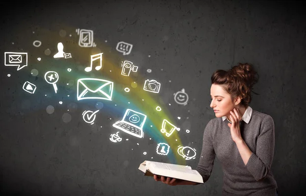 Young woman reading a book with multimedia icons coming out of t — Stock Photo, Image