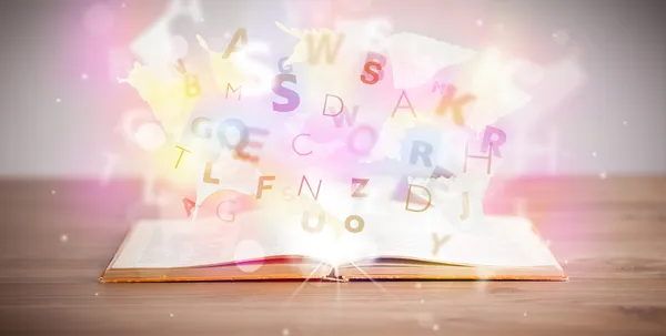 Открытая книга с светящимися буквами на бетонном фоне — стоковое фото