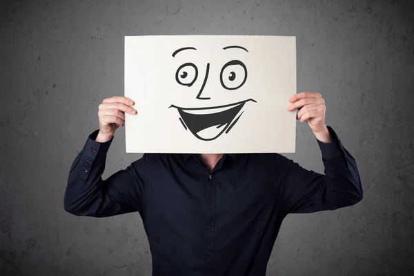 Businessman holding a cardboard with smiley face on it in front — Stock Photo, Image