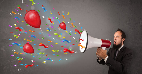 Young guy having fun, shouting into megaphone with balloons