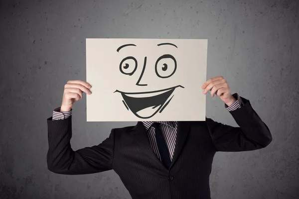 Businessman holding a cardboard with smiley face on it in front — Stock Photo, Image