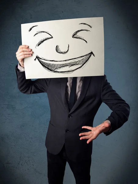 Бізнесмен тримає папір з усміхненим обличчям перед своїм обличчям — стокове фото