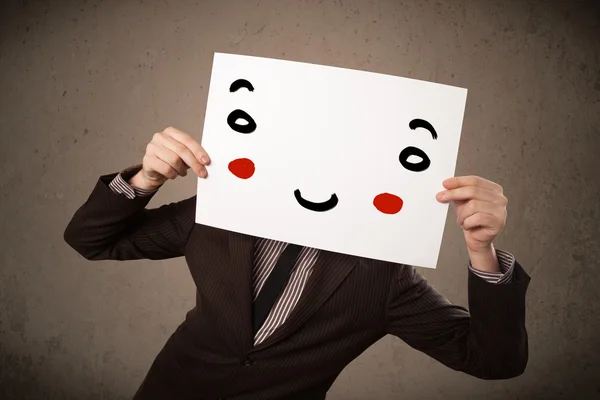 Επιχειρηματίας κρατώντας ένα χαρτόνι με ένα χαμογελαστό πρόσωπο σε αυτό — Φωτογραφία Αρχείου