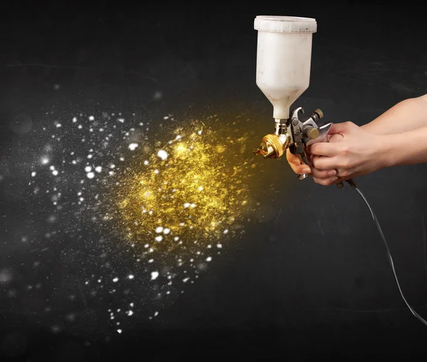 Worker with airbrush painting with glowing golden paint — Stock Photo, Image