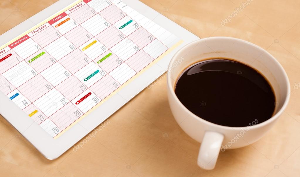 Tablet pc showing calendar on screen with a cup of coffee on a d