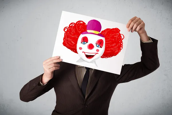 Businessman holding a cardboard with a clown on it in front of h — Stock Photo, Image