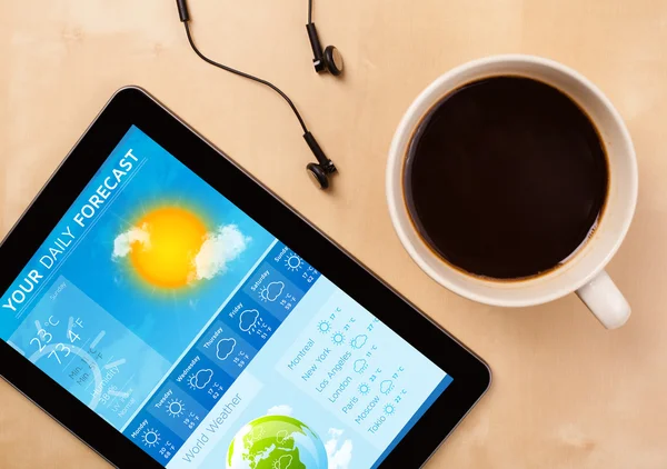 Tablet pc showing weather forecast on screen with a cup of coffe — Stock Photo, Image