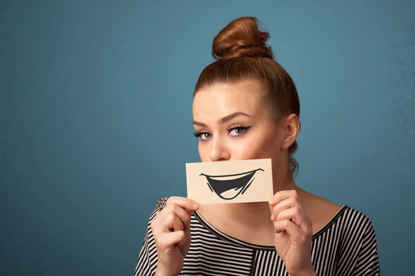 Happy cute girl holding paper with funny smiley drawing — Stock Photo, Image