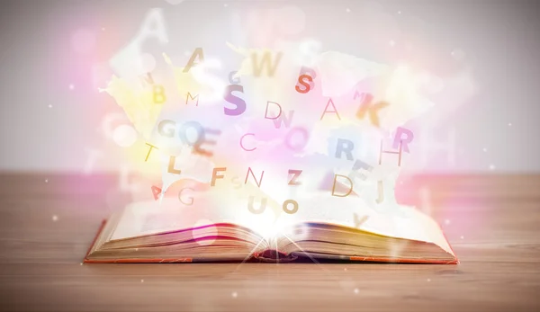 Open book with glowing letters on concrete background — Stock Photo, Image