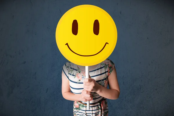 Jovem mulher segurando um emoticon rosto sorridente — Fotografia de Stock