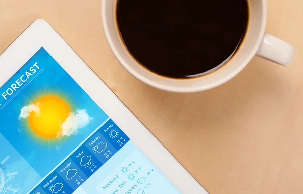 Počítače tablet pc ukazuje předpověď počasí na obrazovce s šálek kafe — Stock fotografie