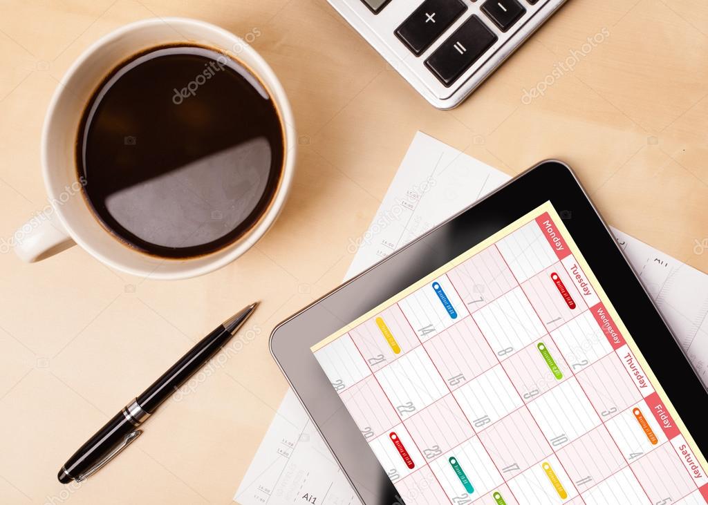 Tablet pc showing calendar on screen with a cup of coffee on a d