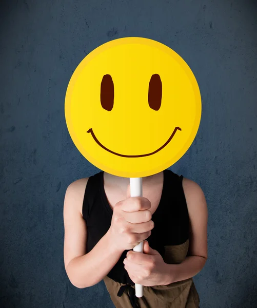 Jovem mulher segurando um emoticon rosto sorridente — Fotografia de Stock
