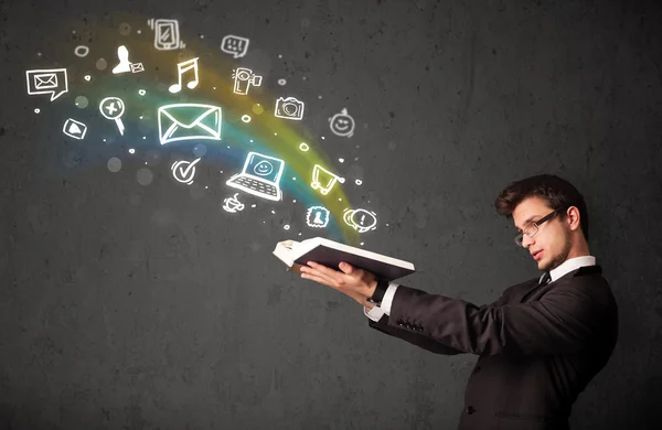 Young businessman reading a book with multimedia icons coming ou — Stock Photo, Image