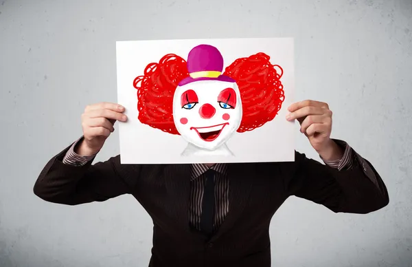 Businessman holding a cardboard with a clown on it in front of h — Stock Photo, Image