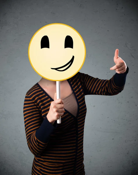 Mujer joven sosteniendo un emoticono sonriente — Foto de Stock