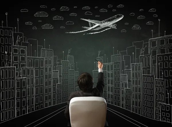 Businessman sitting in front of a cityscape drawing on a chalkbo — Stock Photo, Image