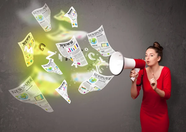 Girl yelling into loudspeaker and newspapers fly out — Stock Photo, Image