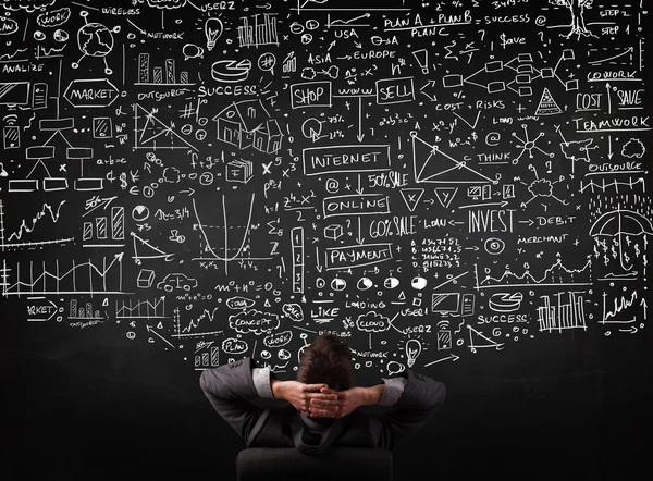 İşadamı elinde çizelgelerle bir tahtanın önünde oturuyor.