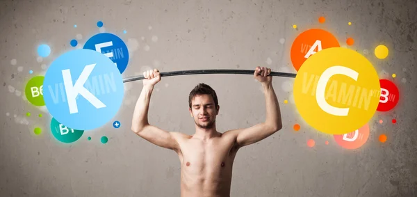 Skinny guy lifting colorful vitamin weights — Stock Photo, Image