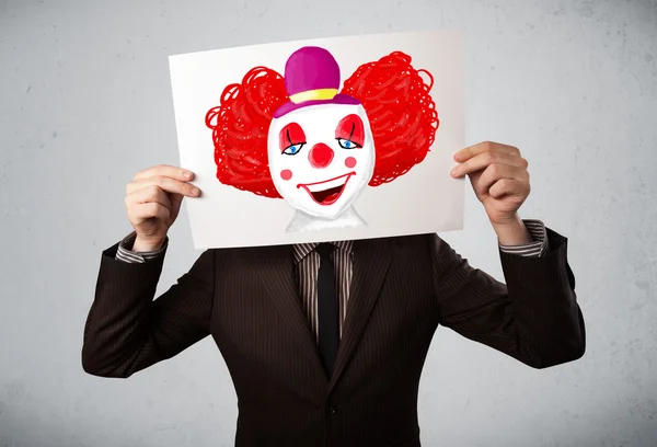 Businessman holding a cardboard with a clown on it in front of h — Stock Photo, Image