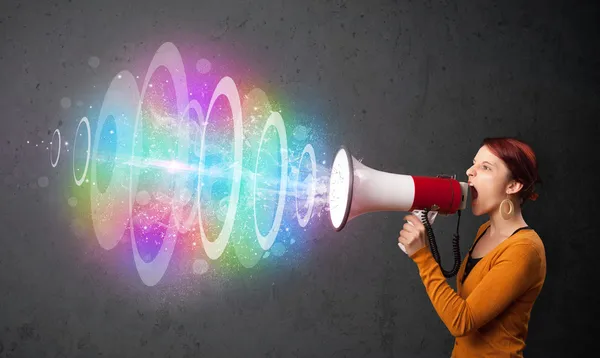 Young girl yells into a loudspeaker and colorful energy beam com — Stock Photo, Image