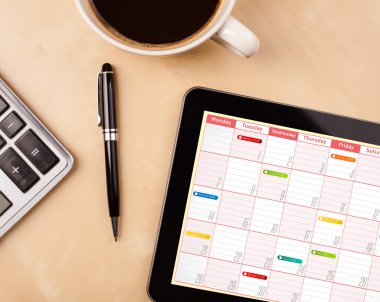 Tablet pc showing calendar on screen with a cup of coffee on a d clipart