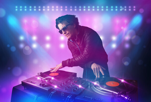 Disc jockey mixing music on turntables on stage with lights and