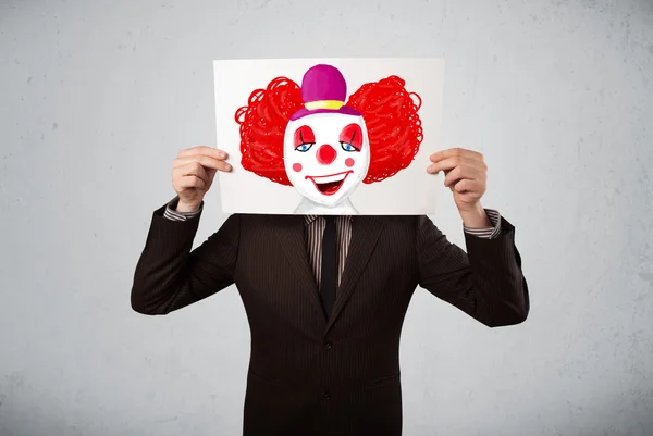 Uomo d'affari in possesso di un cartone con un clown su di esso di fronte h — Foto Stock