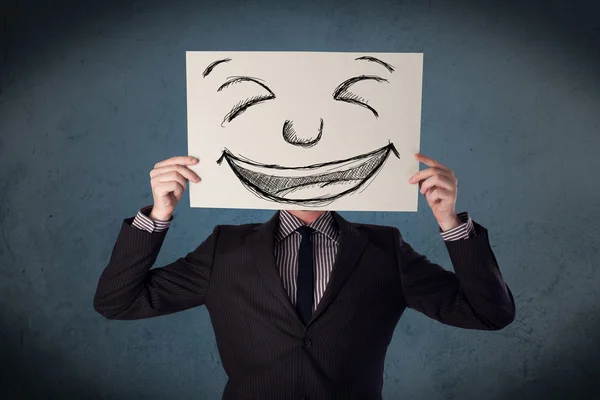 Empresario sosteniendo un papel con la cara sonriente delante de su hea —  Fotos de Stock