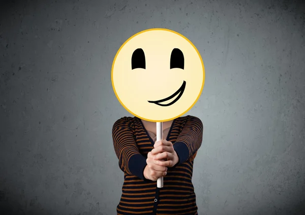 Young woman holding a smiley face emoticon — Stock Photo, Image